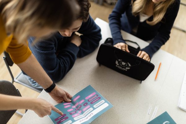 Lärare förklarar en uppgift för två elever.