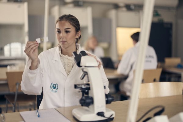 Elev i vit labbrock med ett mikroskop