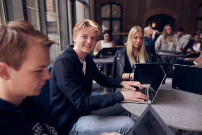 Flera elever med sina datorer i skolans gemensamma lokaler