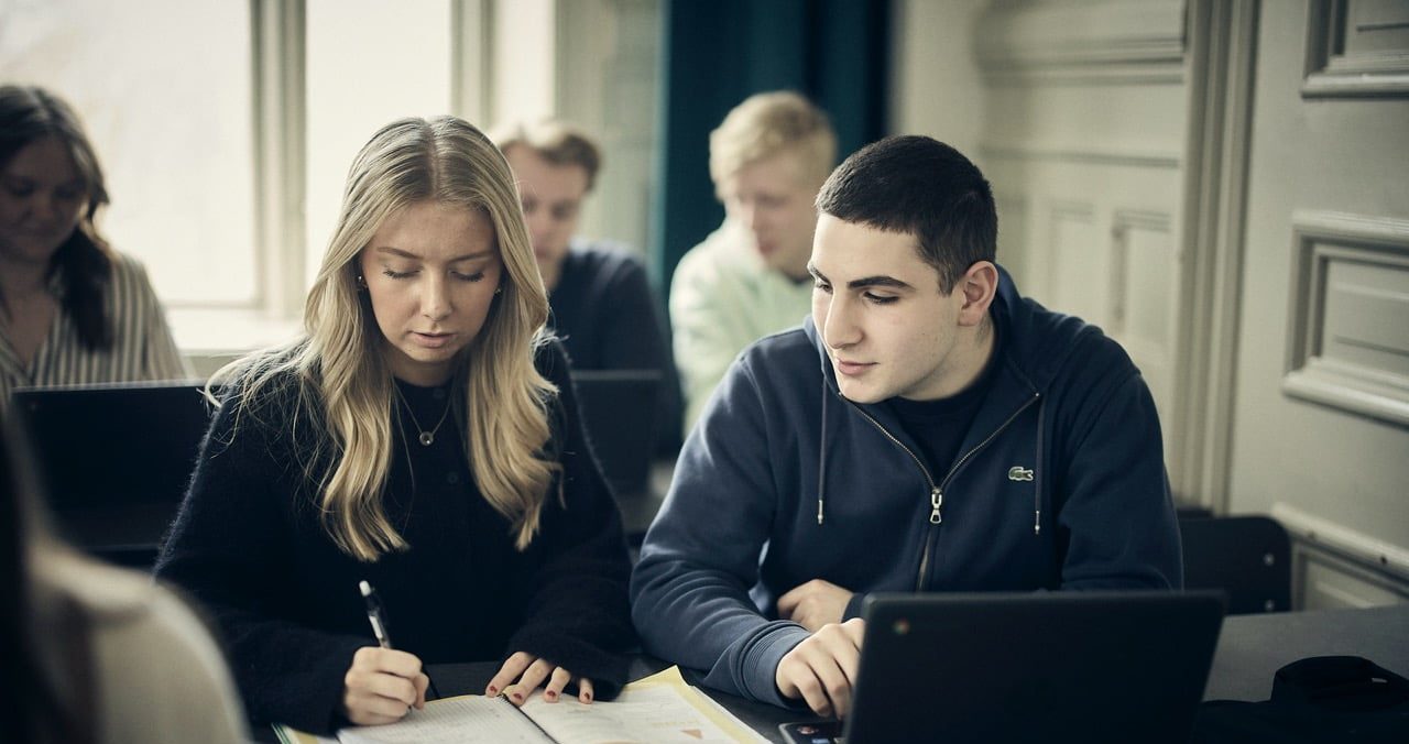 Två elever tittar på en laptop och diskuterar i klassrummet.
