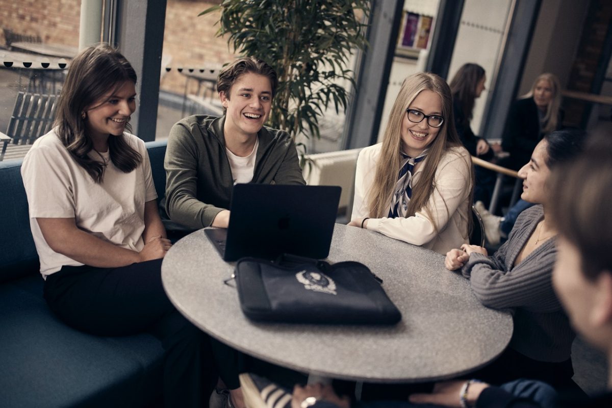 Studenter i samtal kring en bärbar dator i skolans café.