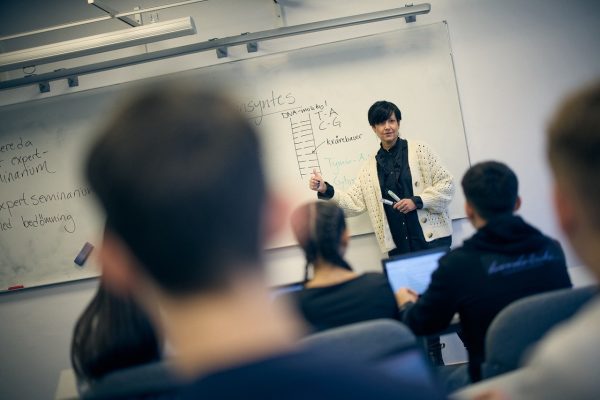 Lärare skriver på tavlan i ett fullt klassrum