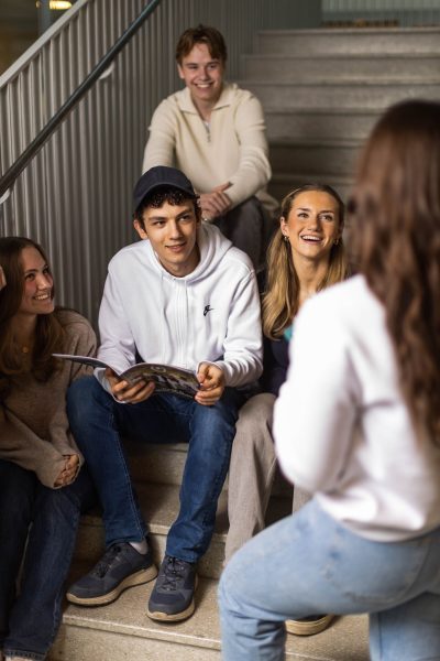 Elever sitter i en av skolans trappor och läser en katalog.