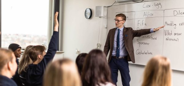 Lärare undervisar framme vid tavlan i ett klassrum.