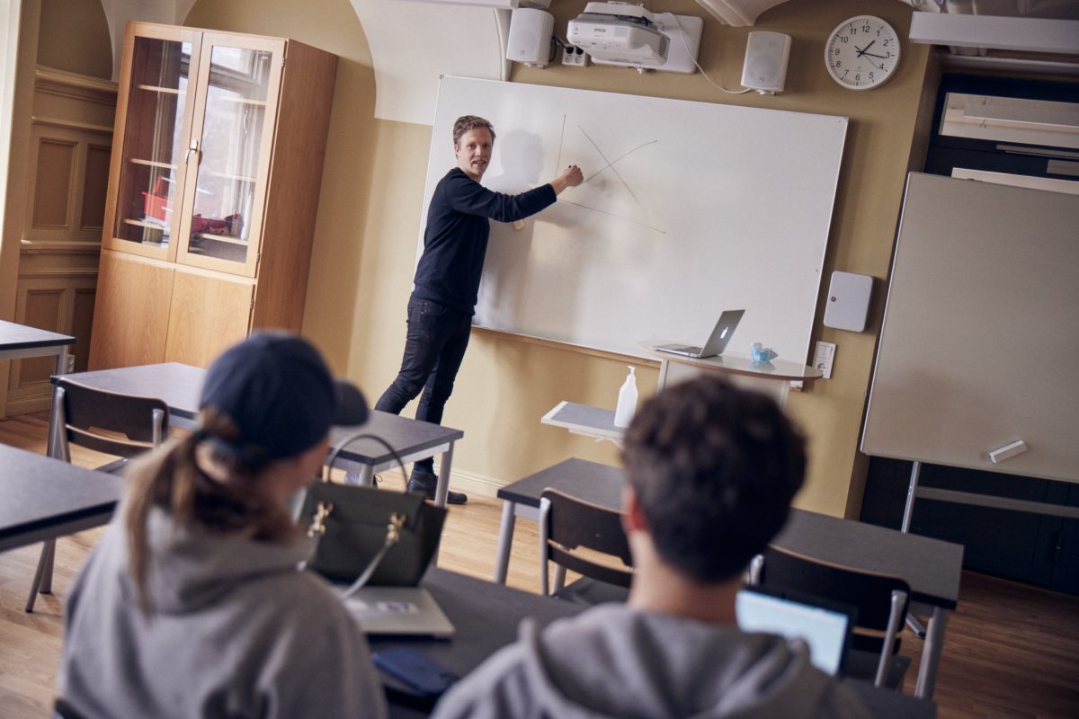 Lärare står vid tavlan och undervisar för elever i ett klassrum.