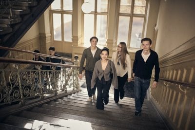 Studenter går uppför en trappa i en historisk skolbyggnad.