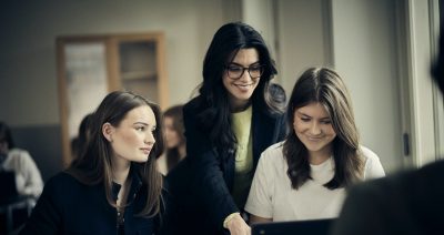 Lärare hjälper elever med uppgifter på en laptop i klassrummet.