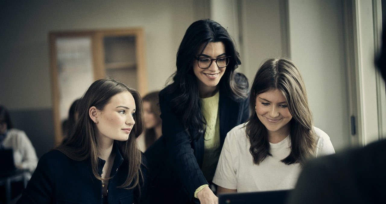 Lärare hjälper elever med uppgifter på en laptop i klassrummet.