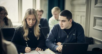 Två elever tittar på en laptop och diskuterar i klassrummet.