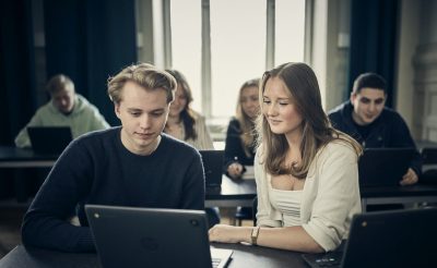 Två elever i labbrockar använder mikroskop i ett laboratorium.