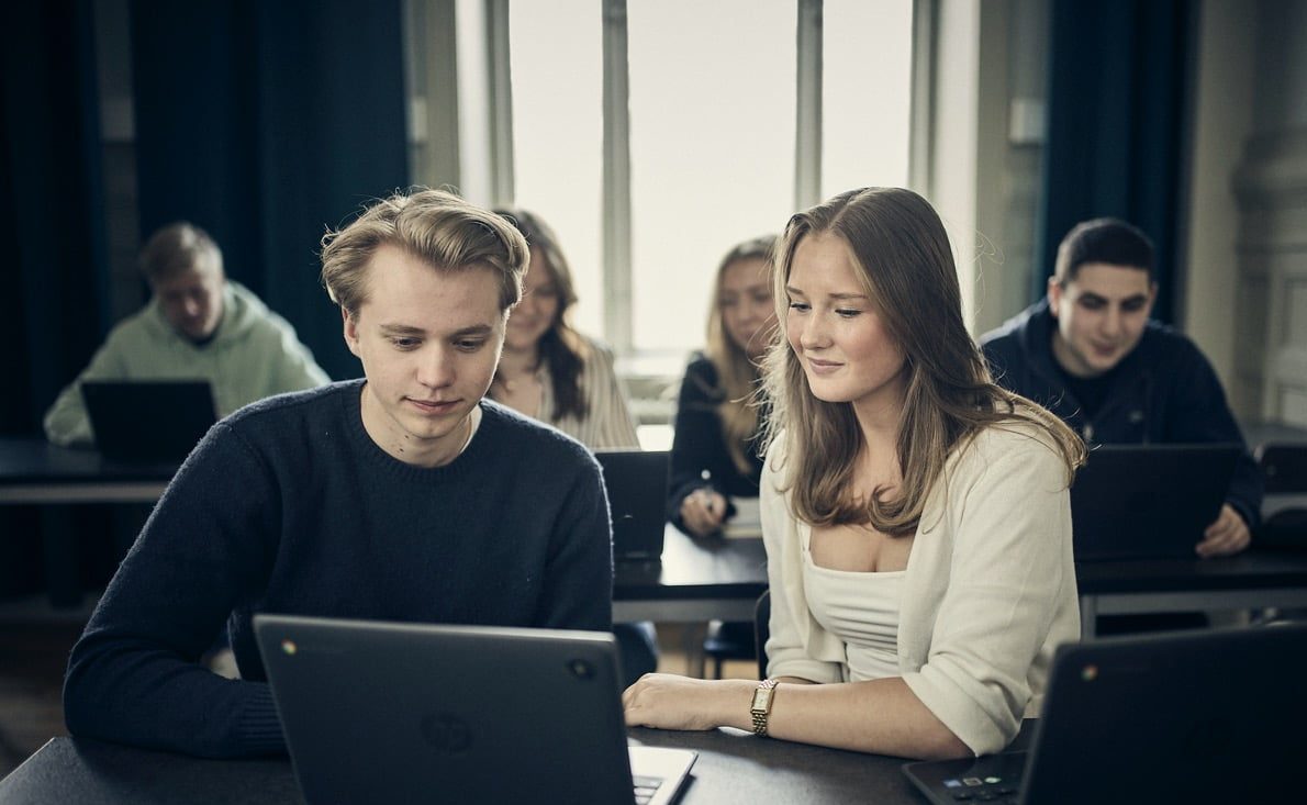 Två elever i labbrockar använder mikroskop i ett laboratorium.