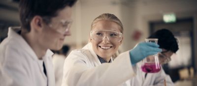 Lärare pratar med två elever som studerar tillsammans i klassrummet.