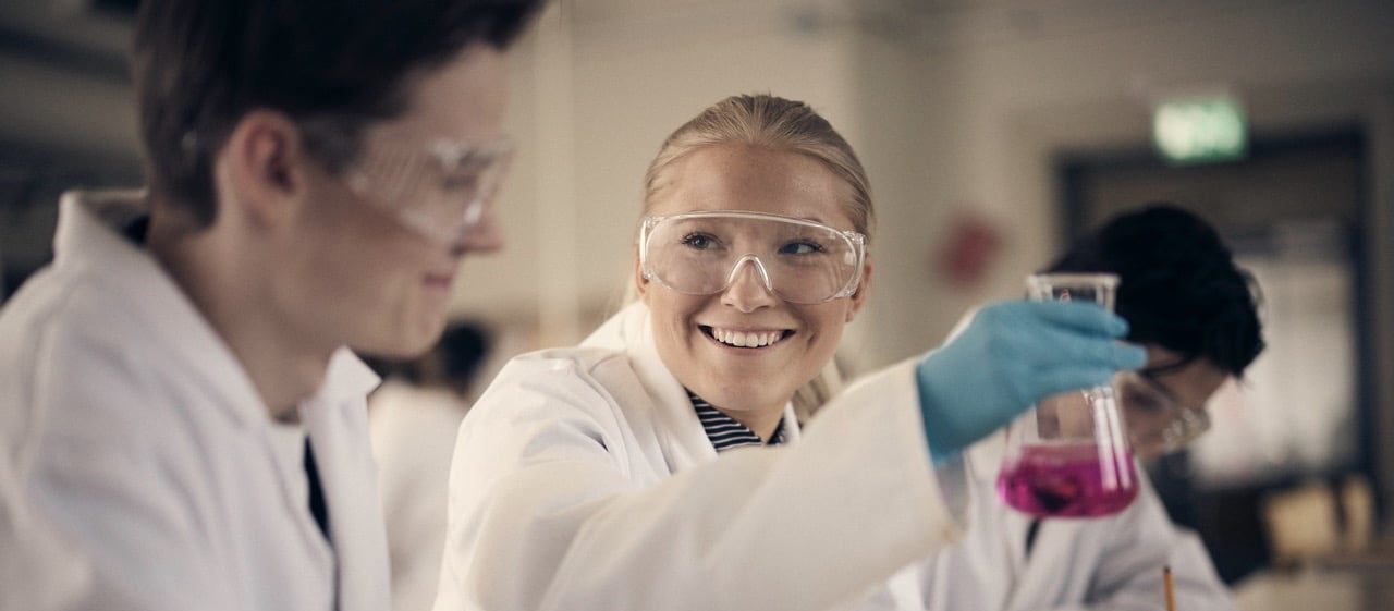 Lärare pratar med två elever som studerar tillsammans i klassrummet.