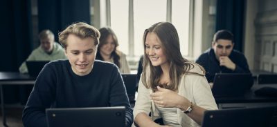 Två elever samarbetar och ler medan de tittar på en laptop i klassrummet.