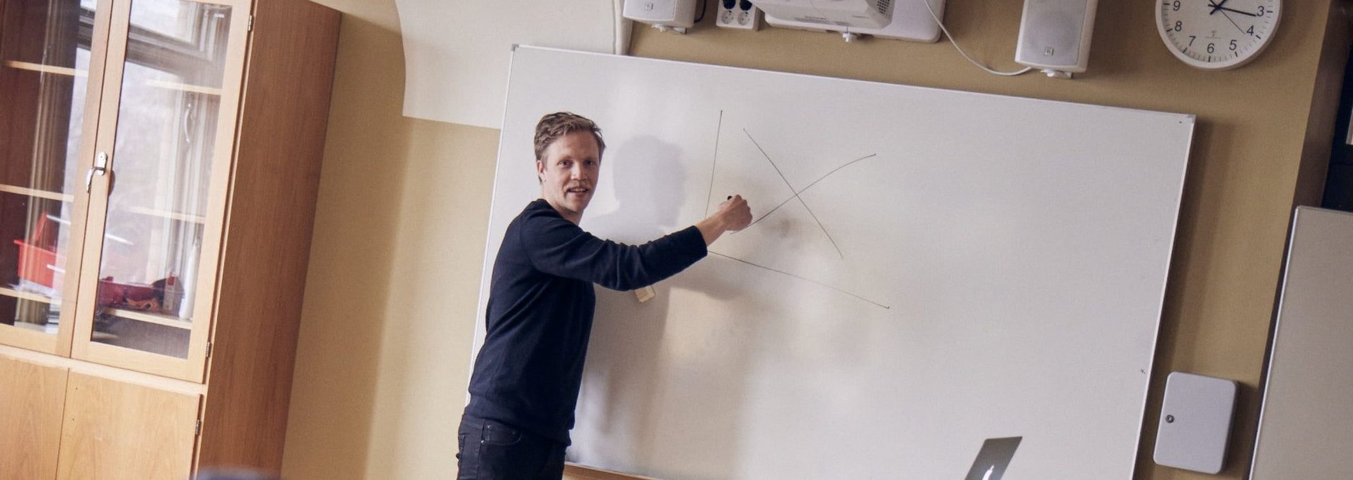 Lärare undervisar framme vid tavlan i ett klassrum.