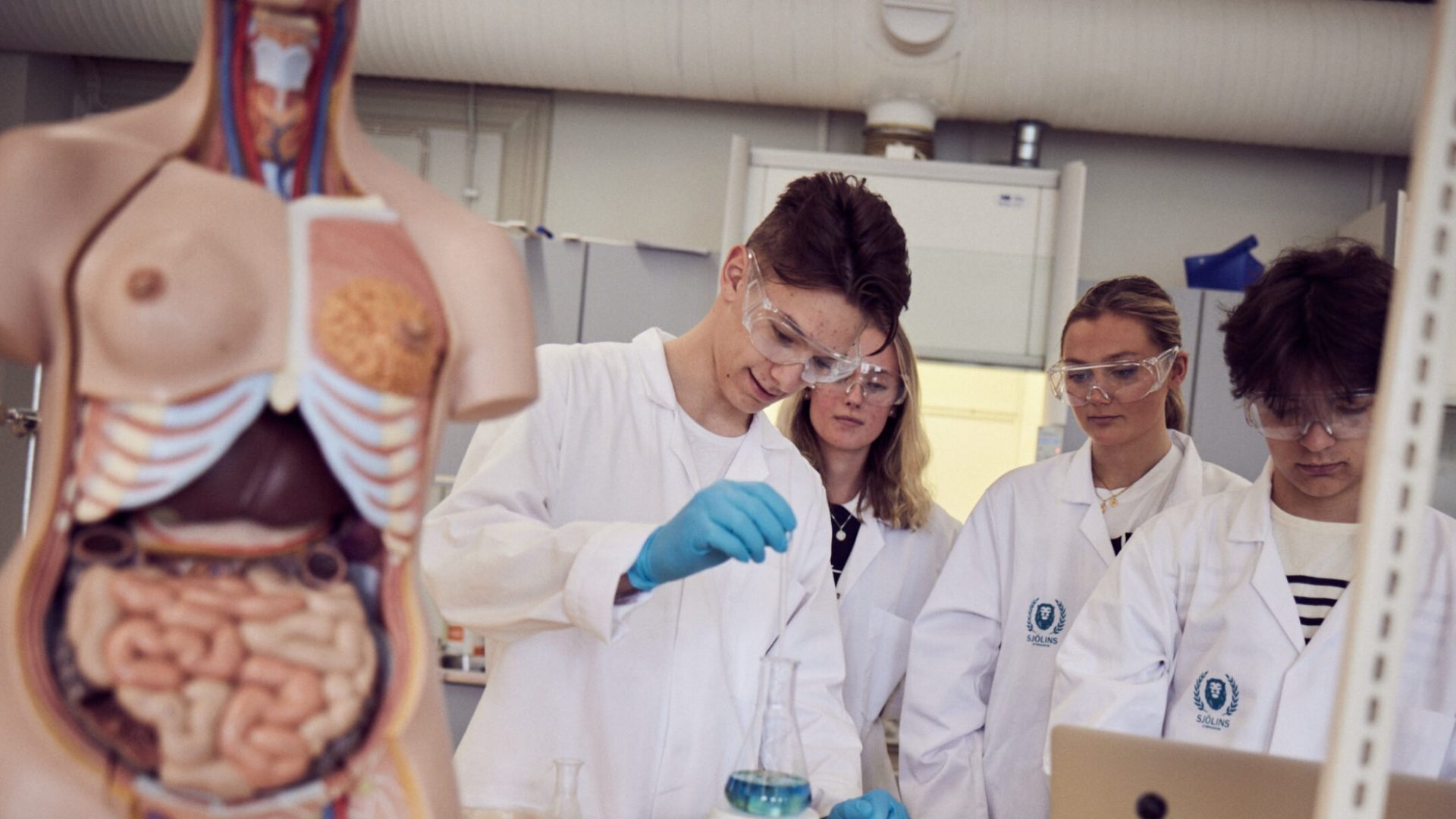 Elever med vita rockar och skyddsglasögon laborerar