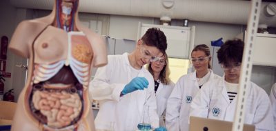 Elever med vita rockar och skyddsglasögon laborerar