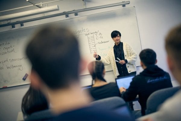 Lärare skriver på tavlan i ett fullt klassrum.