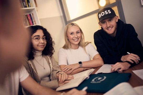 Tre elever sitter runt ett bord i skolans gemensamma lokaler.