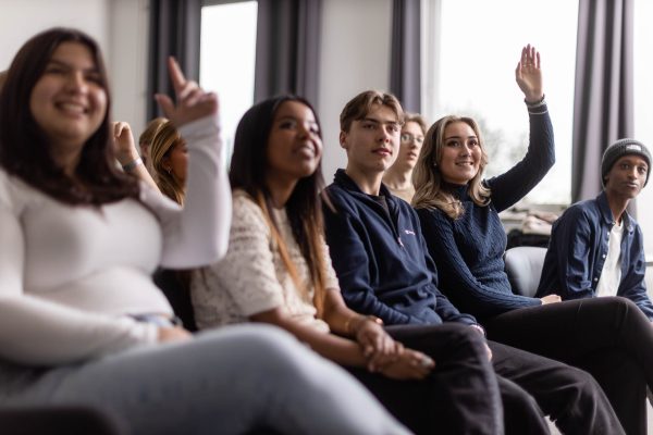Elever sitter i ett klassrum och räcker upp sina händer