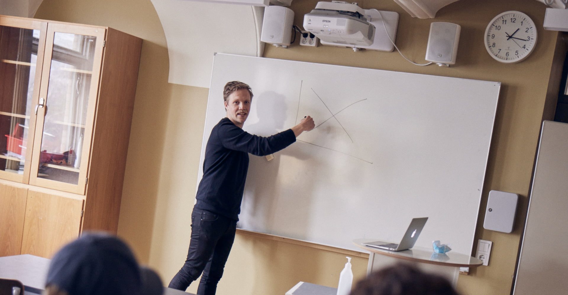 Lärare undervisar framme vid tavlan i ett klassrum.