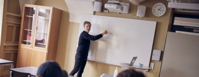 Lärare undervisar framme vid tavlan i ett klassrum.