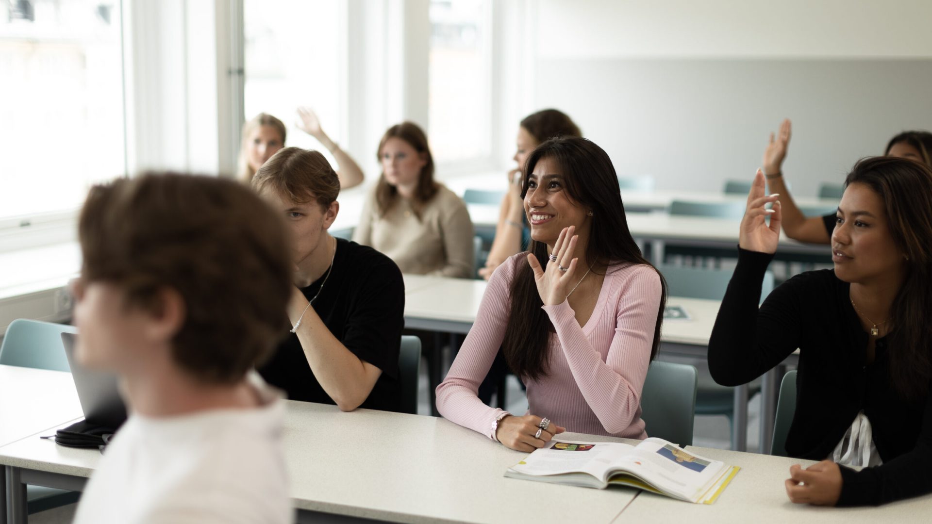 Elever sitter i ett klassrum och räcker upp sina händer