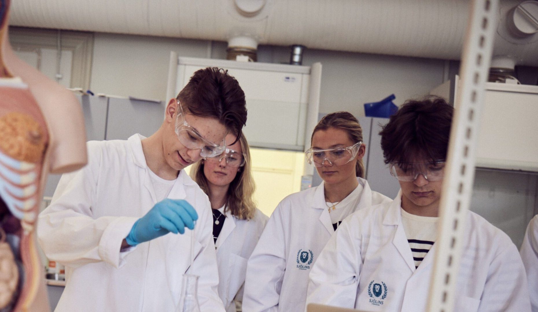 Elever med vita rockar och skyddsglasögon laborerar