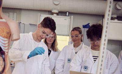 Elever med vita rockar och skyddsglasögon laborerar