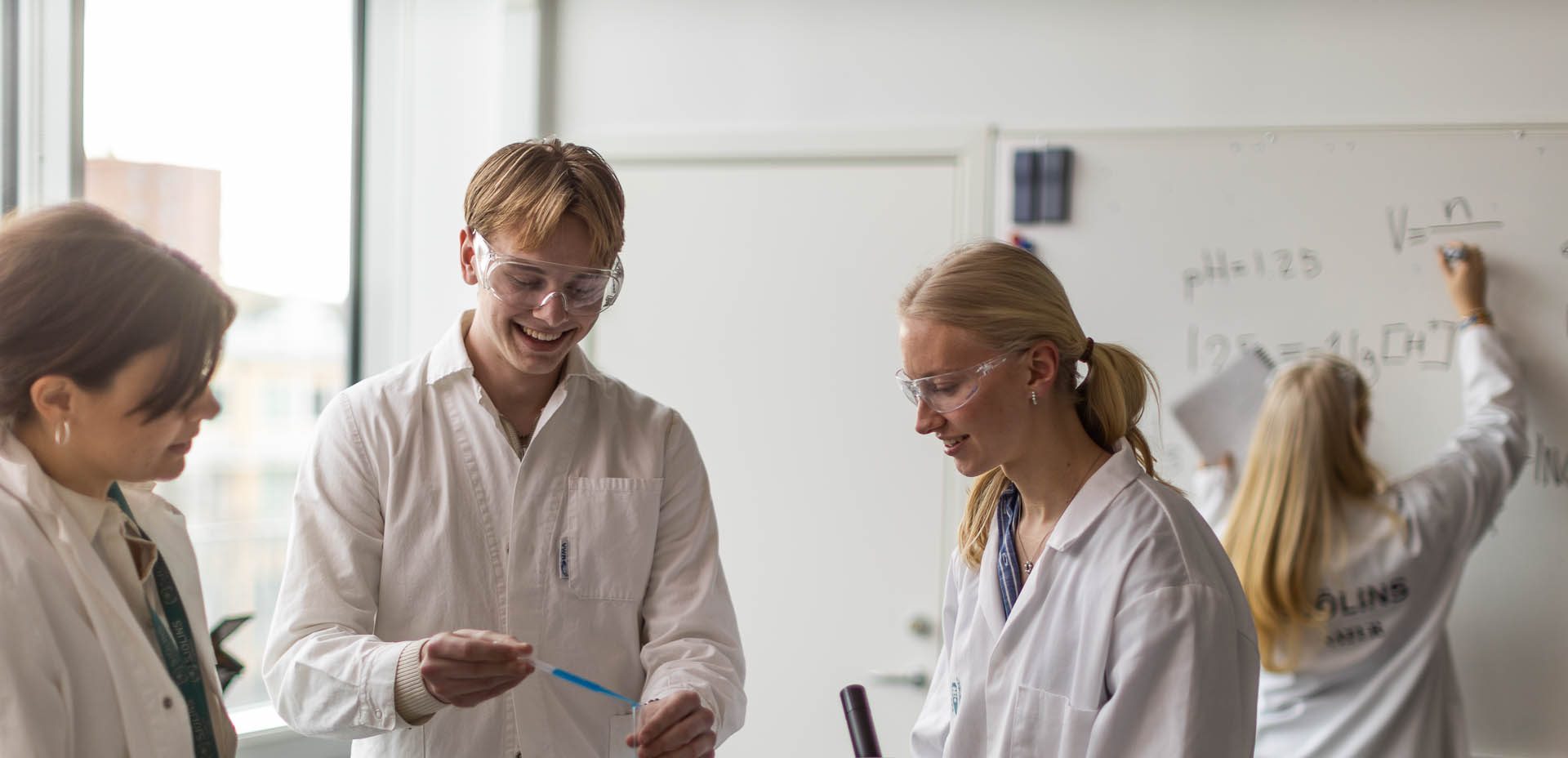 Elever med vita rockar och skyddsglasögon laborerar