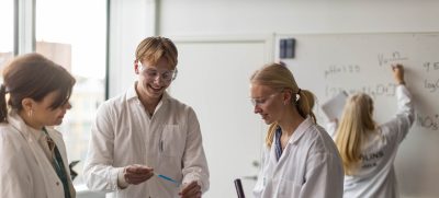 Elever med vita rockar och skyddsglasögon laborerar