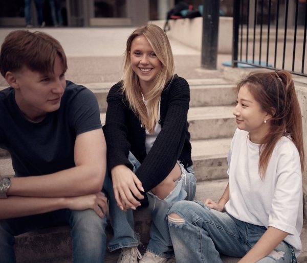 Tre glada elever som sitter i en trappa och pratar.
